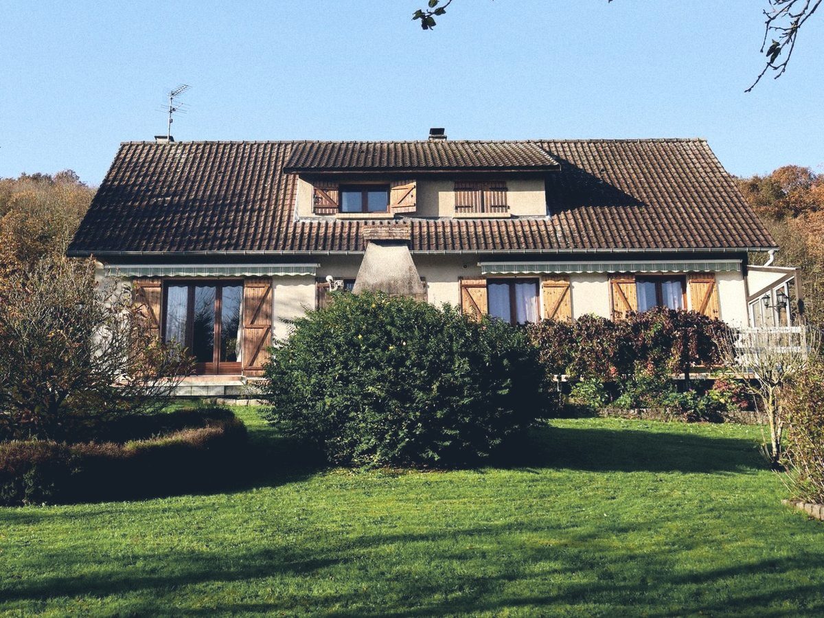 Landhuis met bruine luiken achter een ruime tuin in het najaar
