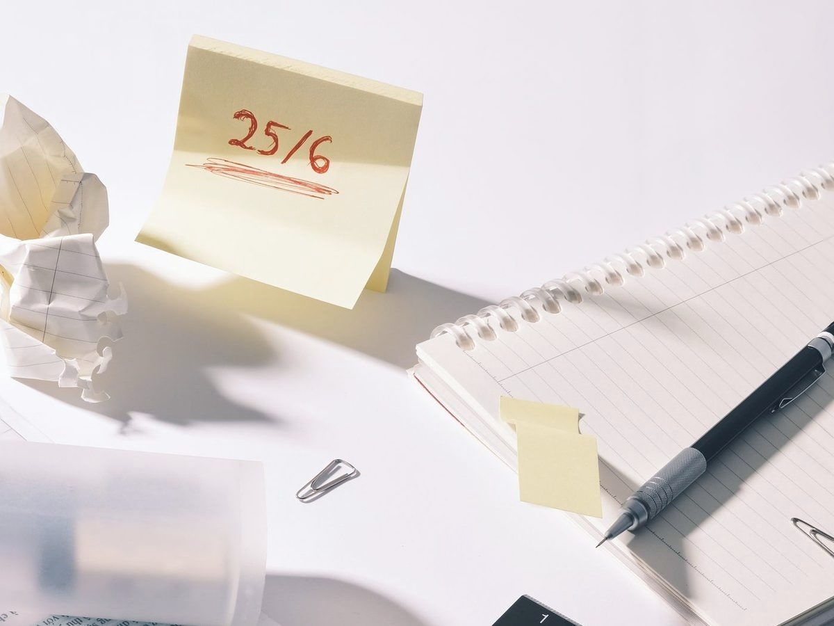 Bureau van bovenaf met een gele post-it waarop een datum staat, een notitieblok en een pen