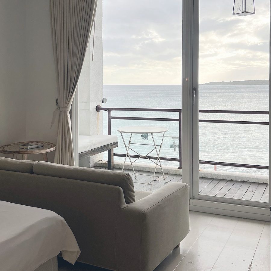 Lichte woonkamer met zicht op zee door een openslaande deur, met een klein bistrotafeltje op het terras